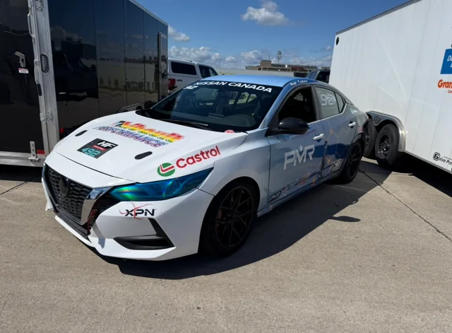 Voiture de course HF Racing aux couleurs de Castrol et XPN, dans le paddock